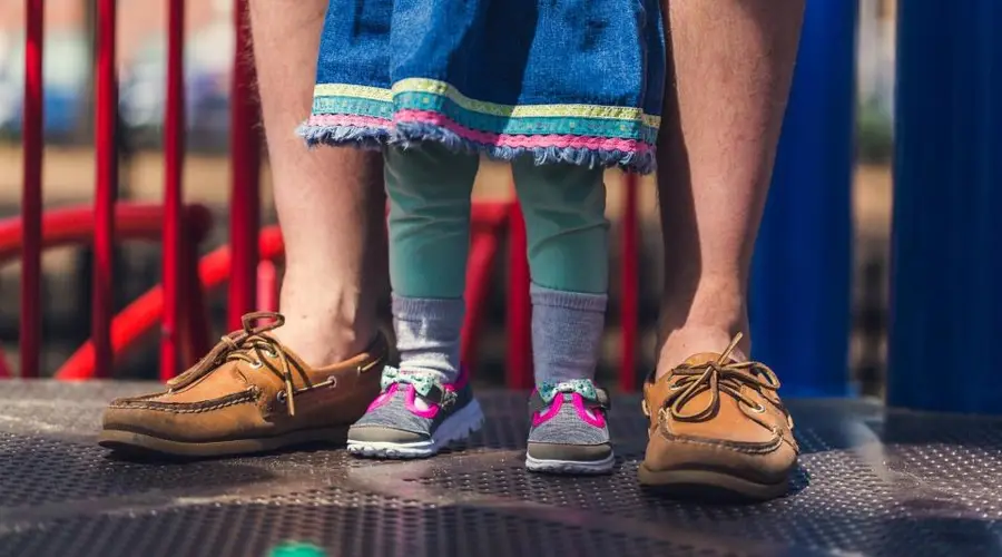 Criança de tênis infantil entre os pés de um adulto